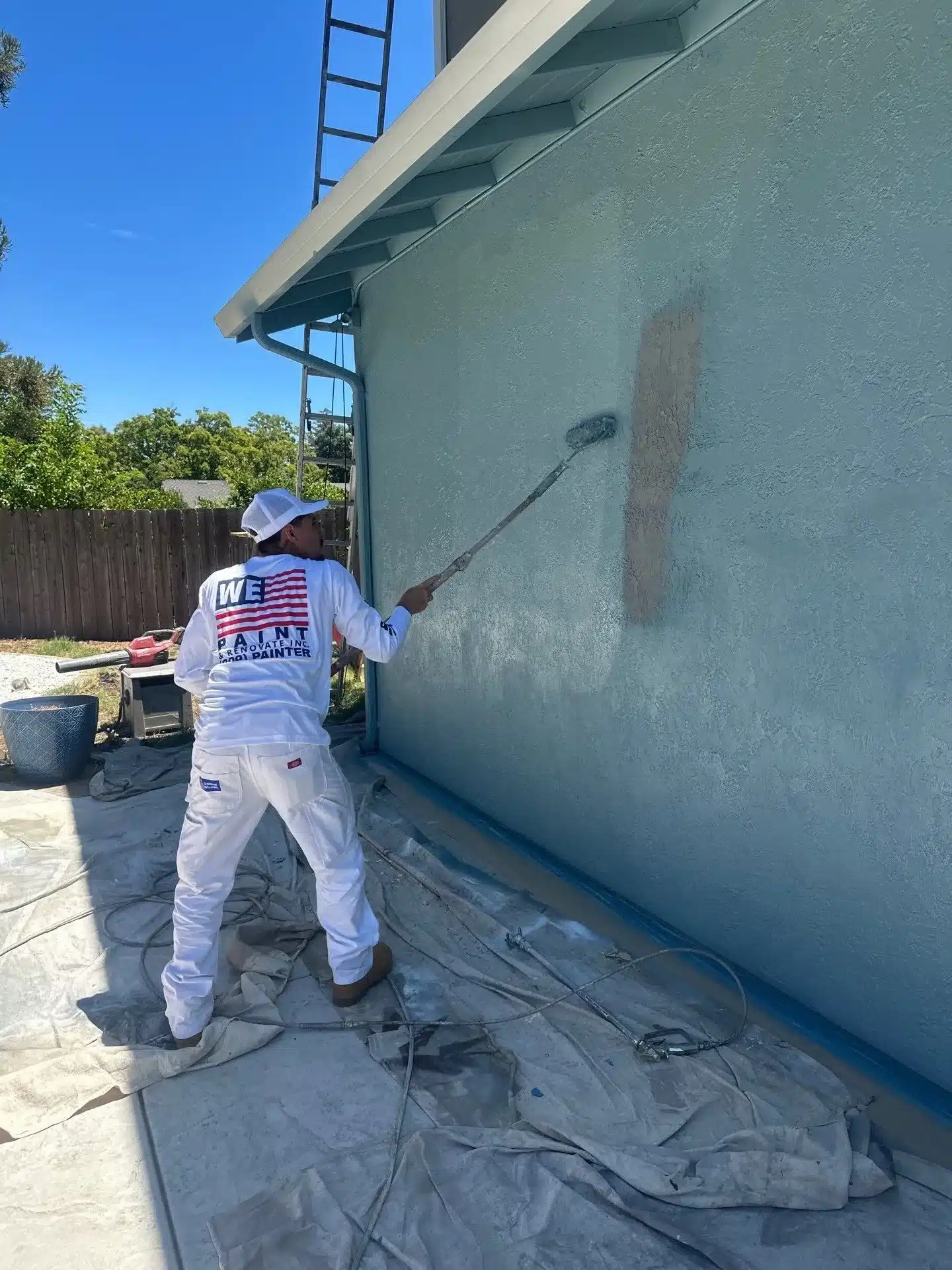 Commercial Exterior Wall Painting Painter in white uniform applying teal paint to weathered commercial building exterior wall in Stockton