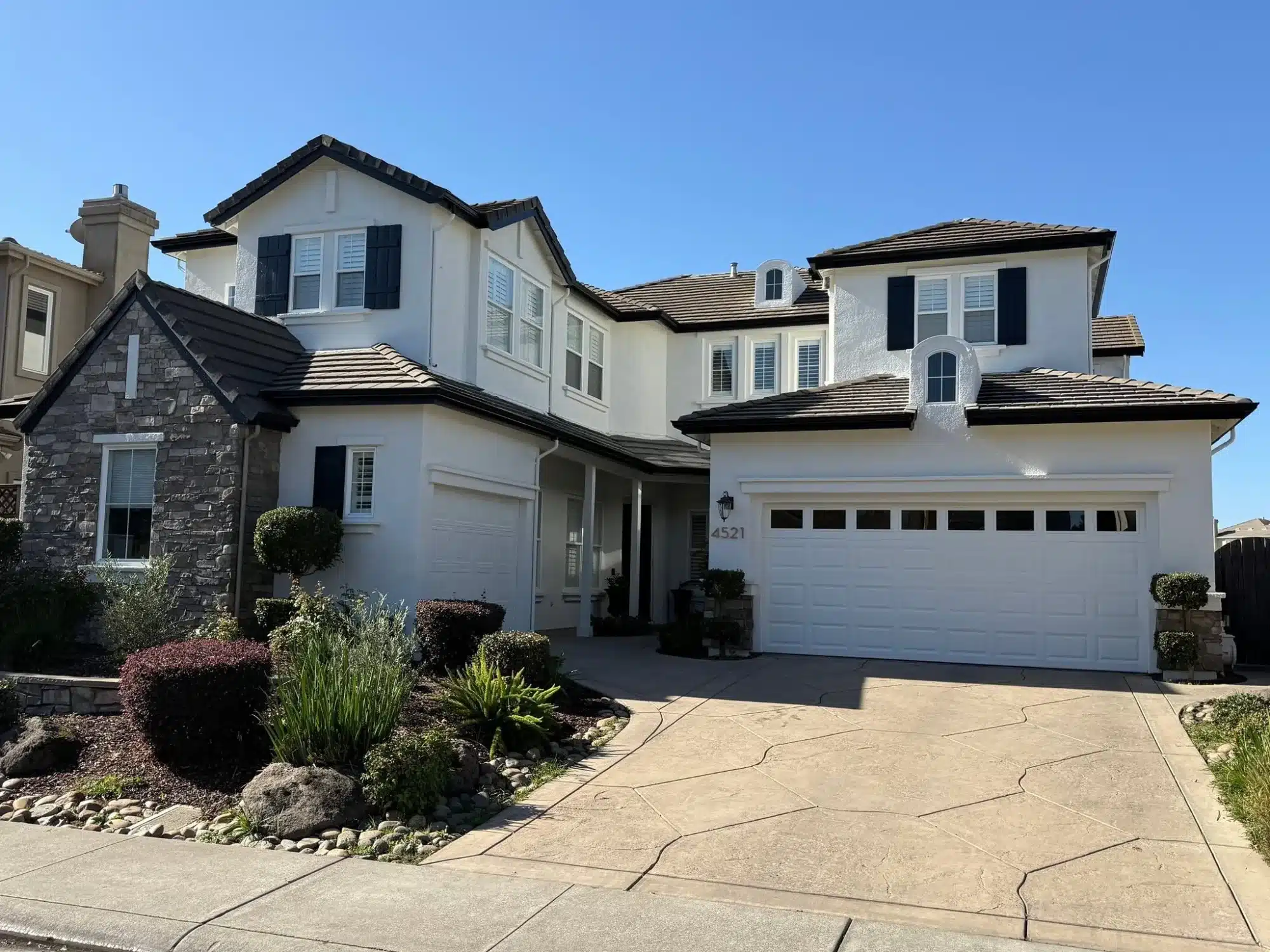 White Exterior Residential Home White-painted two-story residential home with black roof, black shutters, white garage doors, and stone veneer accent wall